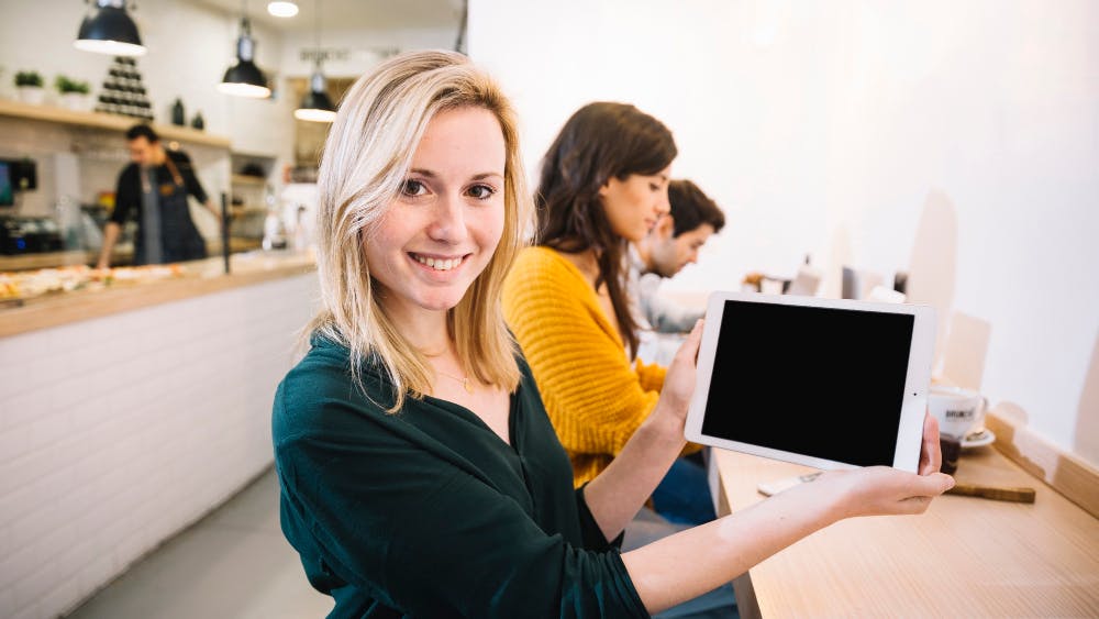 Eine Frau hält ein Tablet mit schwarzem Bildschirm und lächelt in die Kamera.