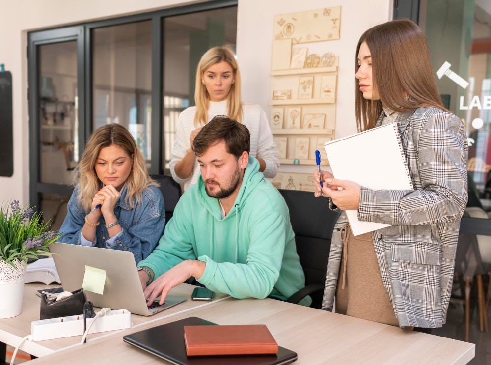 Eine Gruppe von Menschen, die in einem Büro an einem Laptop zusammen arbeiten.