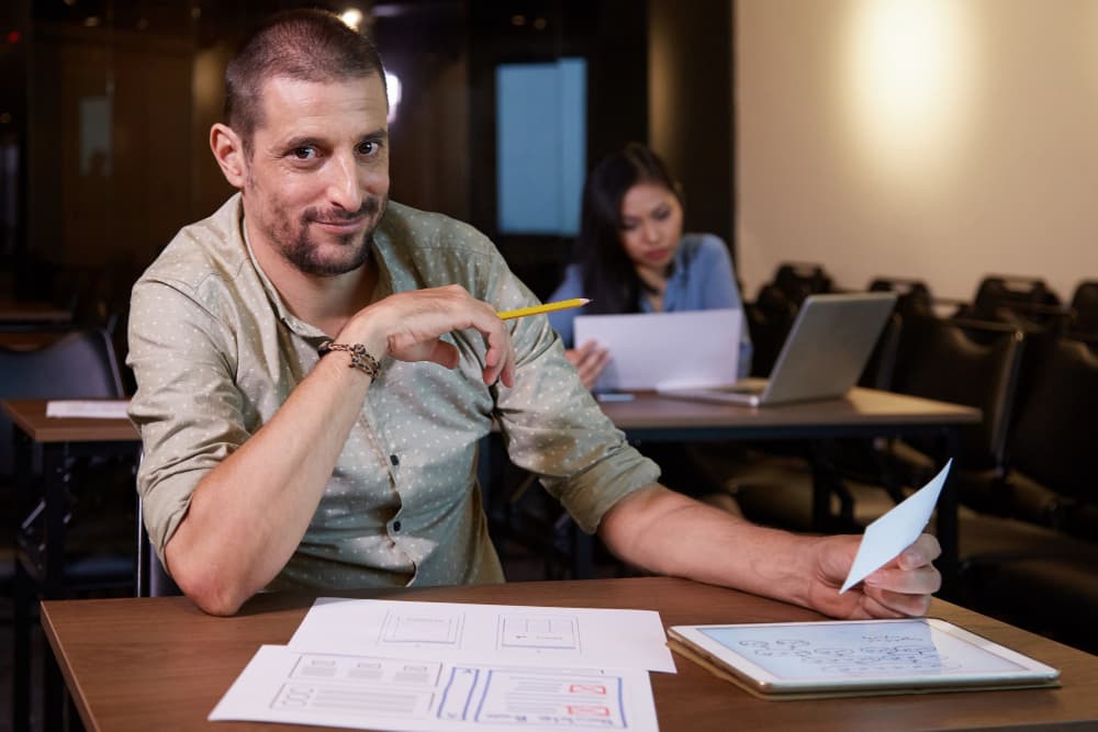 Ein Mann sitzt mit Papieren und einem Bleistift an einem Tisch.