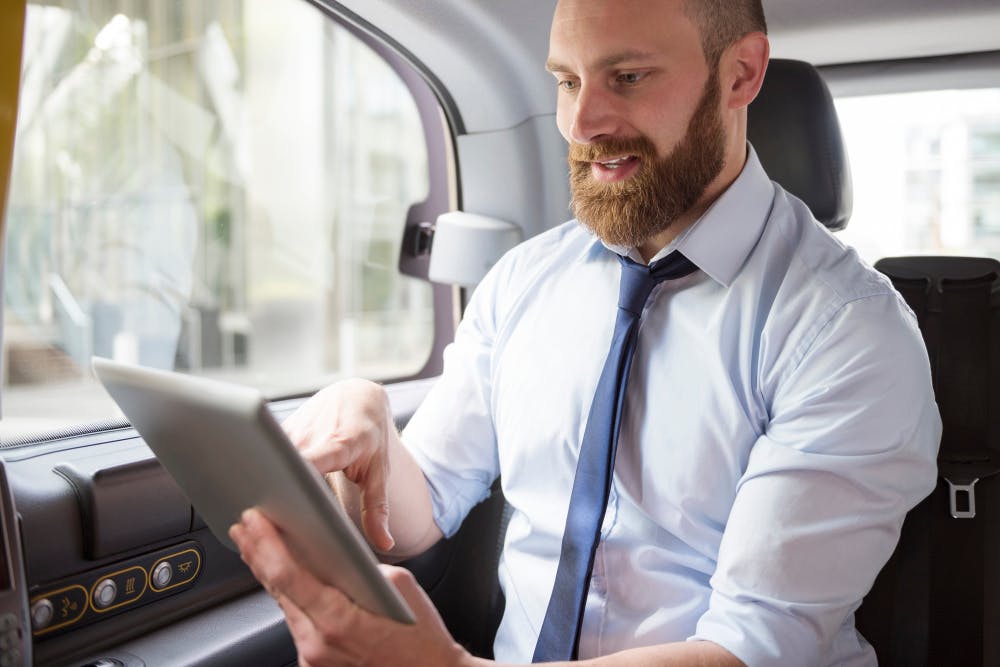 Ein Mann mit Krawatte sitzt in einem Auto und hält ein Tablet in seinen Händen.