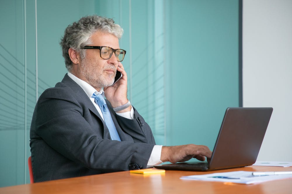 Ein Mann sitzt an vor seinem Laptop und telefoniert.