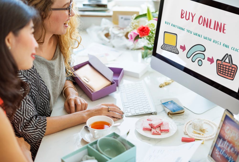 Zwei Frauen schauen auf einen Monitor mit der Aufschrift 'Buy Online'.
