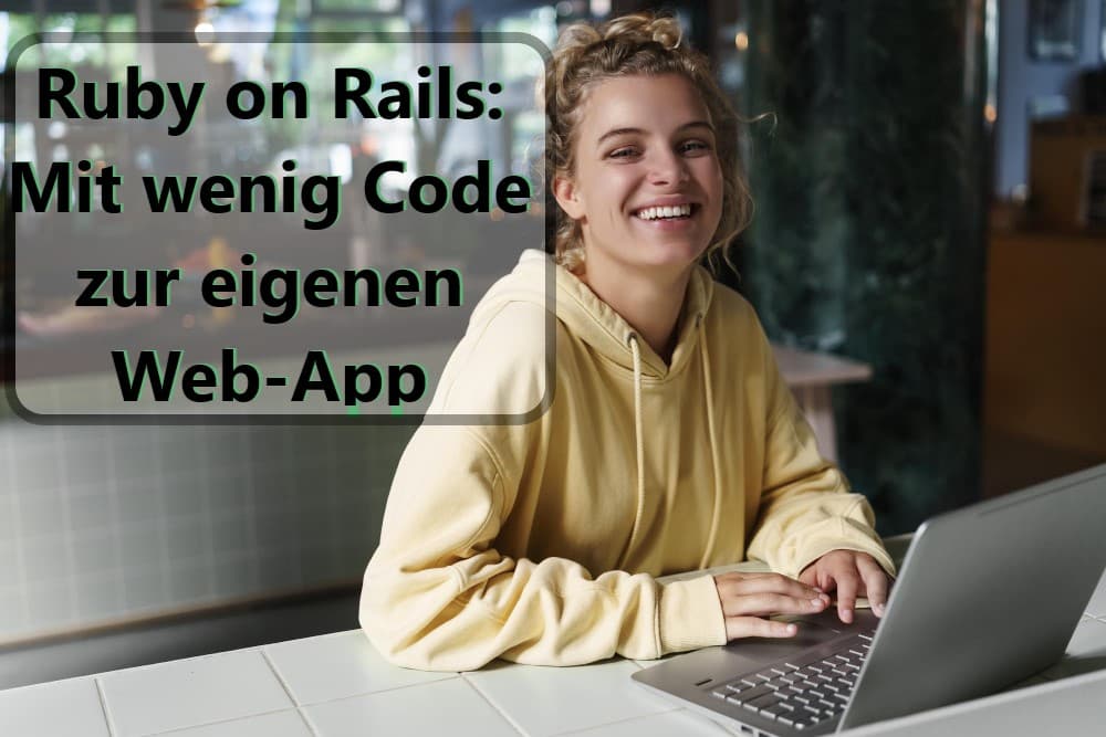 Eine Frau sitzt lächelnd an einem Tisch mit ihrem Laptop.