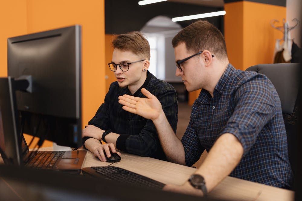 Zwei Personen arbeiten und diskutieren vor einem Computer.