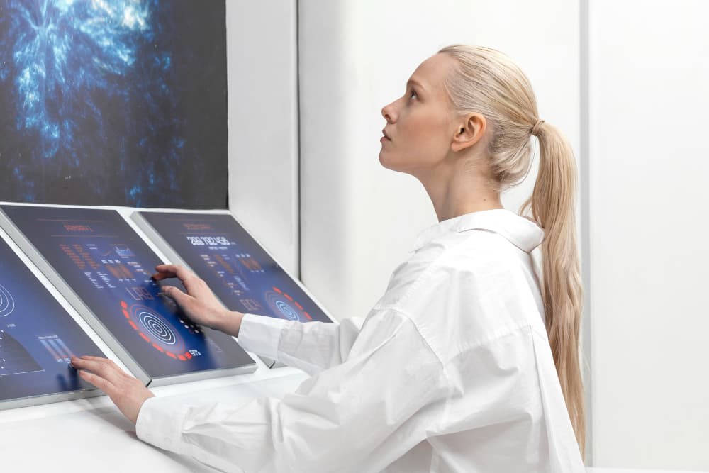 In einem futuristischen Raum bedient eine Frau futuristisch aussehende Touchscreen-Terminals.