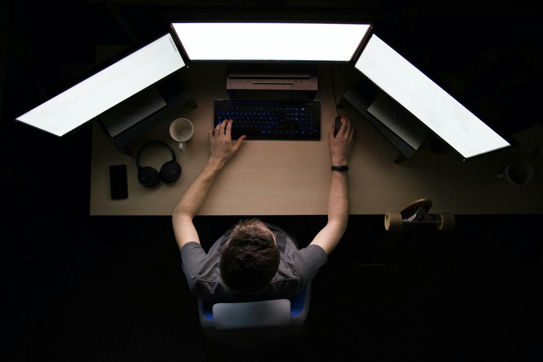 Eine Person arbeitet an einem Schreibtisch mit drei Monitoren aneinander gereiht.