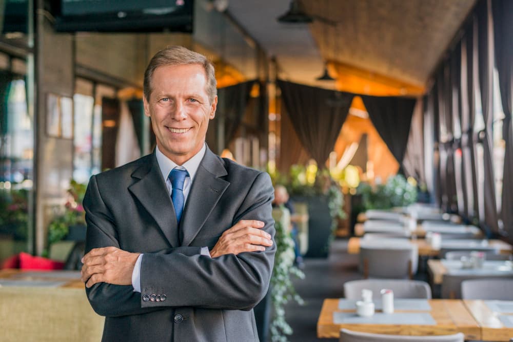 Ein Geschäftsmann im Anzug steht mit verschränkten Armen in einem Restaurant.