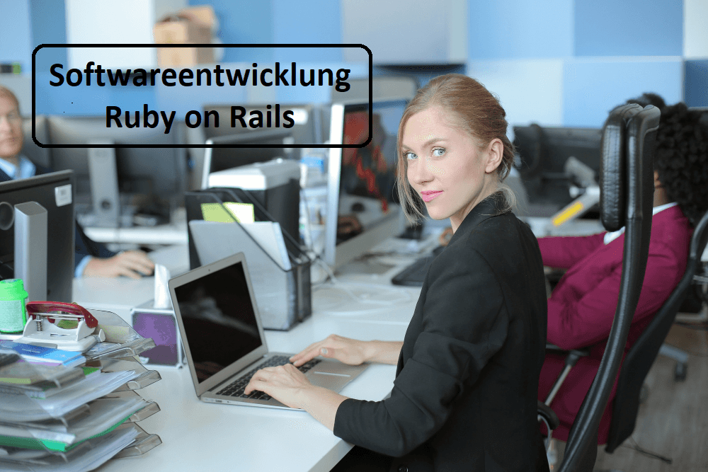 Eine Person sitzt vor einem Laptop und schaut nach links in die Kamera.