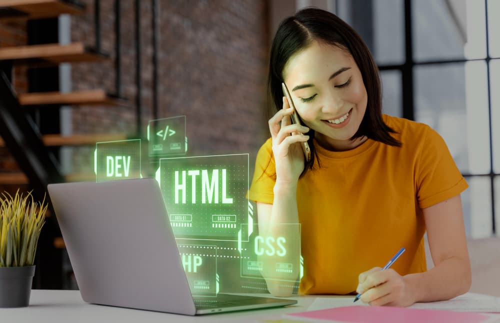 Eine Frau telefoniert, während sie vor einem Laptop mit holographischen HTML- und CSS-Symbolen sitzt.