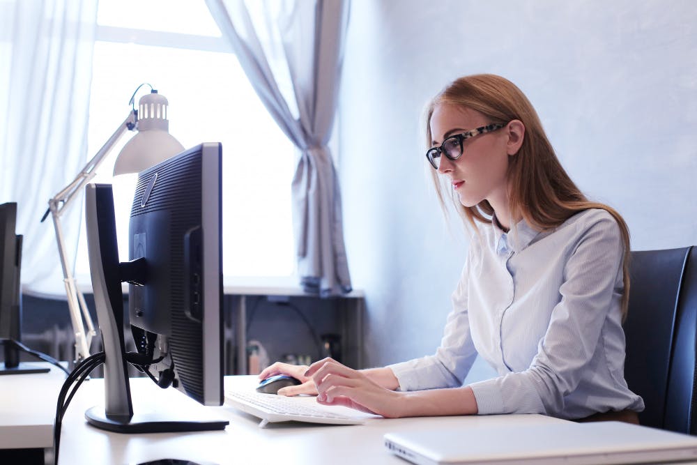 Eine Frau sitzt an einem Schreibtisch und arbeitet konzentriert an ihrem Computer.