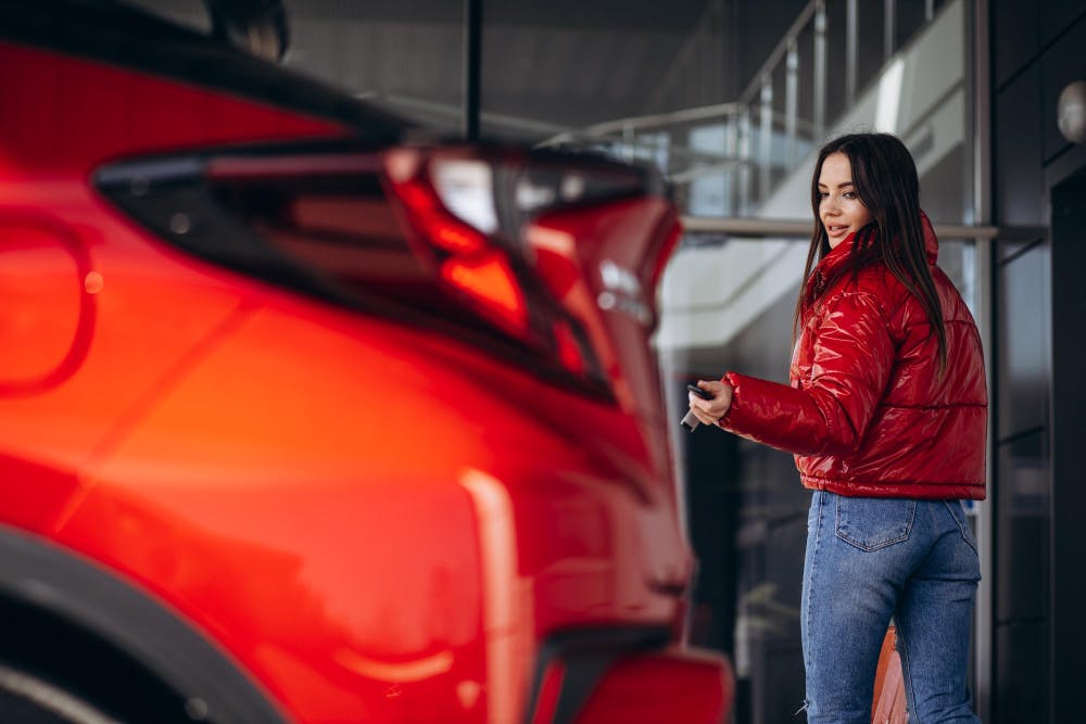 Eine Frau in roter Jacke verriegelt ihr rotes Auto mit dem Autoschlüssel.