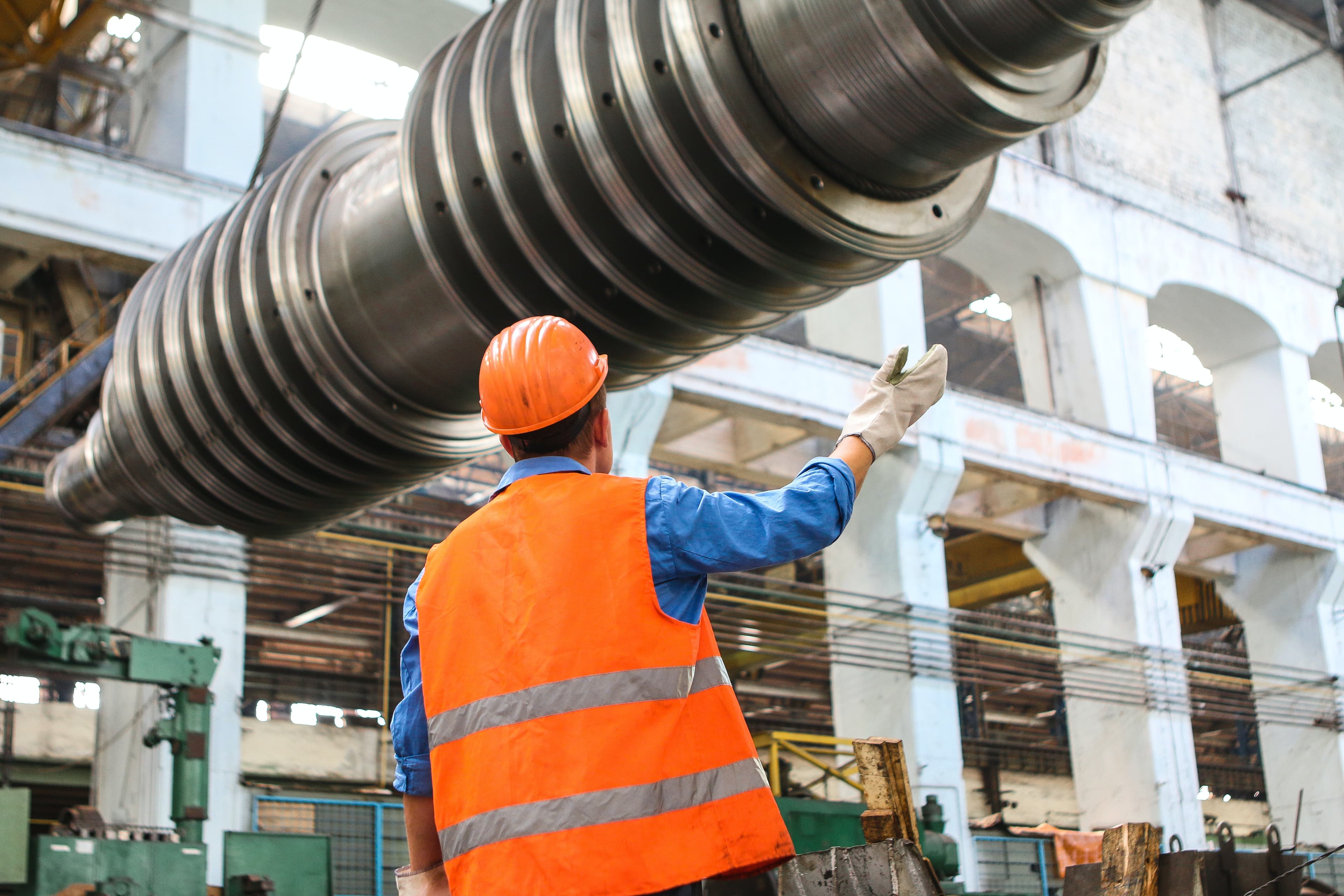 Ein Arbeiter in Warnweste in einer Fabrik prüft ein großes schwebendes Gewinde.