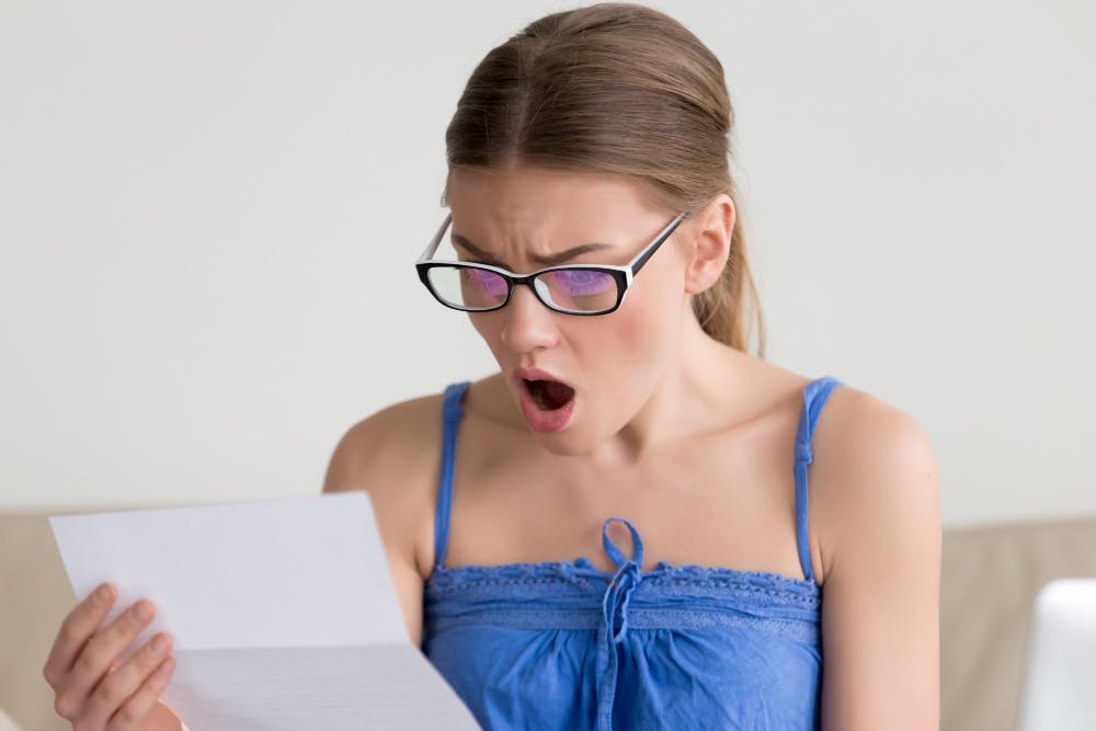 Eine Frau mit Brille schaut schockiert auf einen Zettel, den sie in der Hand hält.