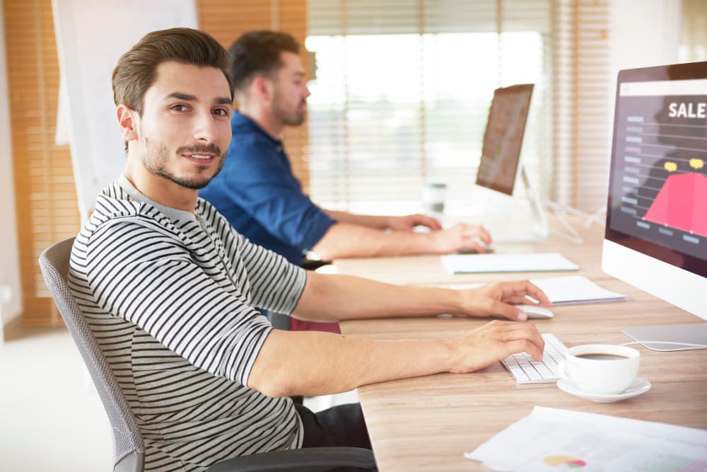 Zwei Personen sitzen an einem Schreibtisch vor ihren Computern.